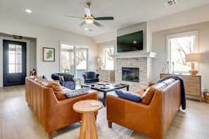 A living room with a sofa set, a coffee table, a fireplace, and a television mounted on the wall. - Steps From the Water! Grand Lake Getaway w/ Patio (Afton)