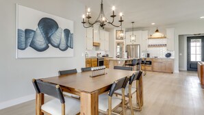A spacious dining area with a wooden table and chairs, a chandelier, and a large abstract painting on the wall. - Steps From the Water! Grand Lake Getaway w/ Patio (Afton)