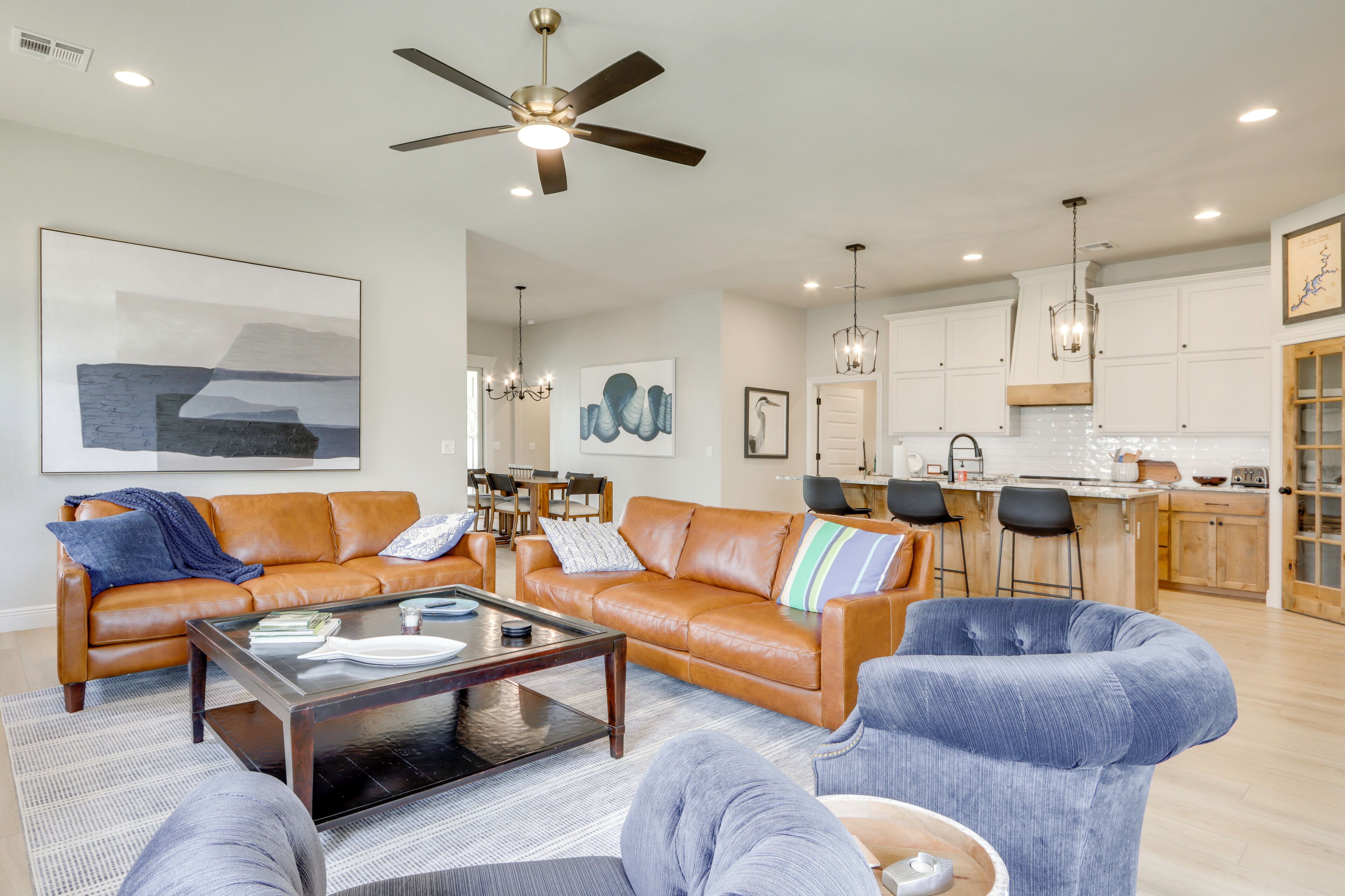 A spacious living room with a large brown leather sofa, a glass coffee table, and a blue armchair.