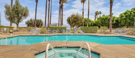 A swimming pool with a hot tub, surrounded by palm trees and lounge chairs.