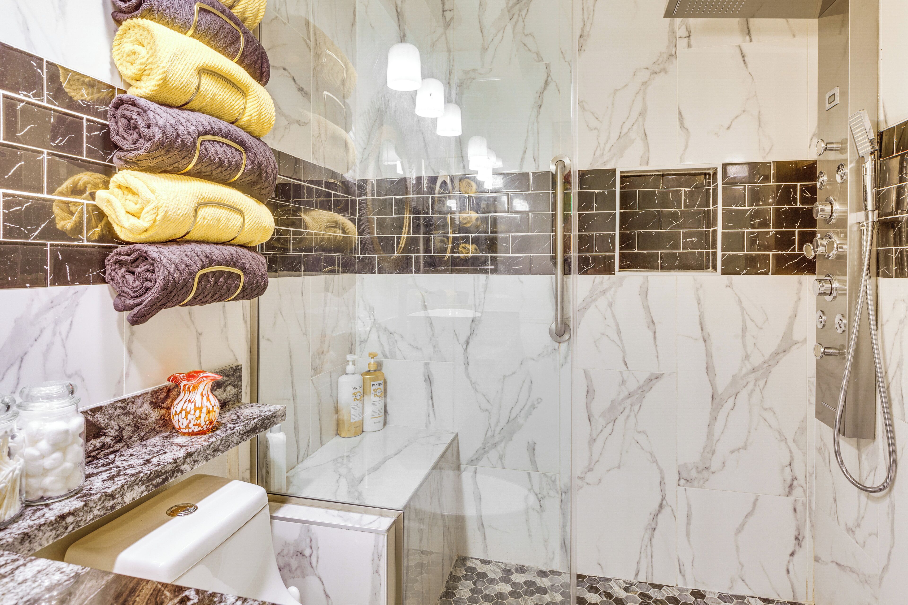 A bathroom with marble walls, a glass shower enclosure, and towels on a rack.