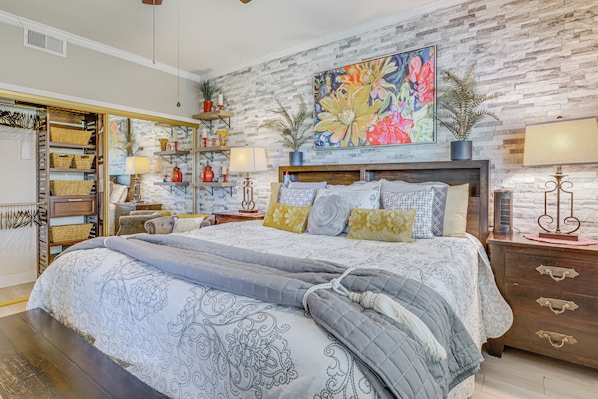 A bedroom with a large bed, a brick-patterned wall, a colorful painting, and a wooden dresser.