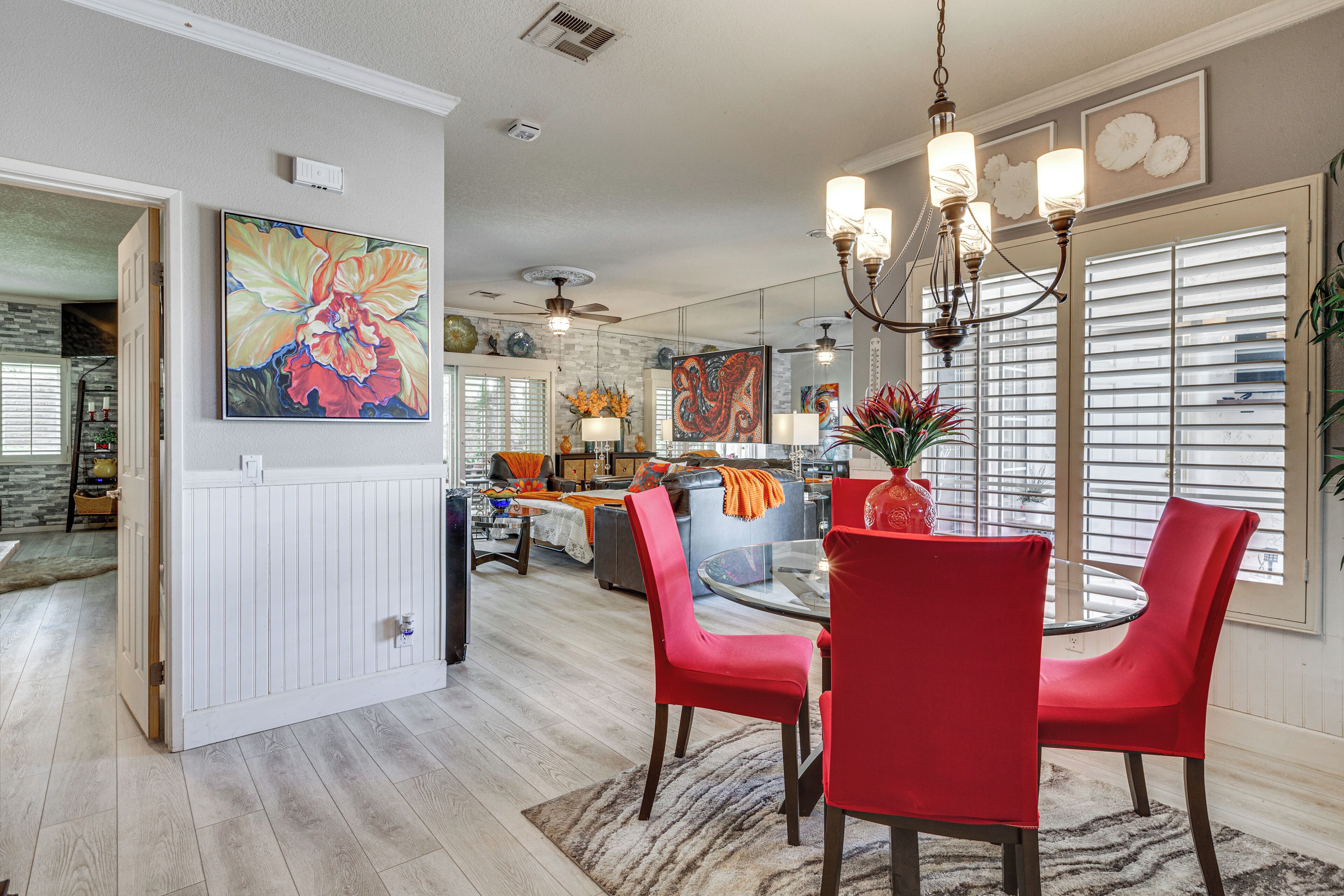 A dining area with a glass table, red chairs, and a chandelier.