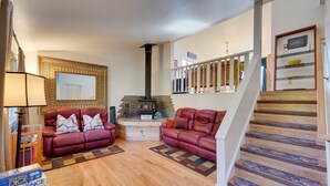 A living room with two red leather sofas, a wooden coffee table, and a fireplace. A staircase with wooden steps and a railing is visible. - < 1 Mi to Pioneer Ave: Homer Base w/ Fire Pit! (Homer)