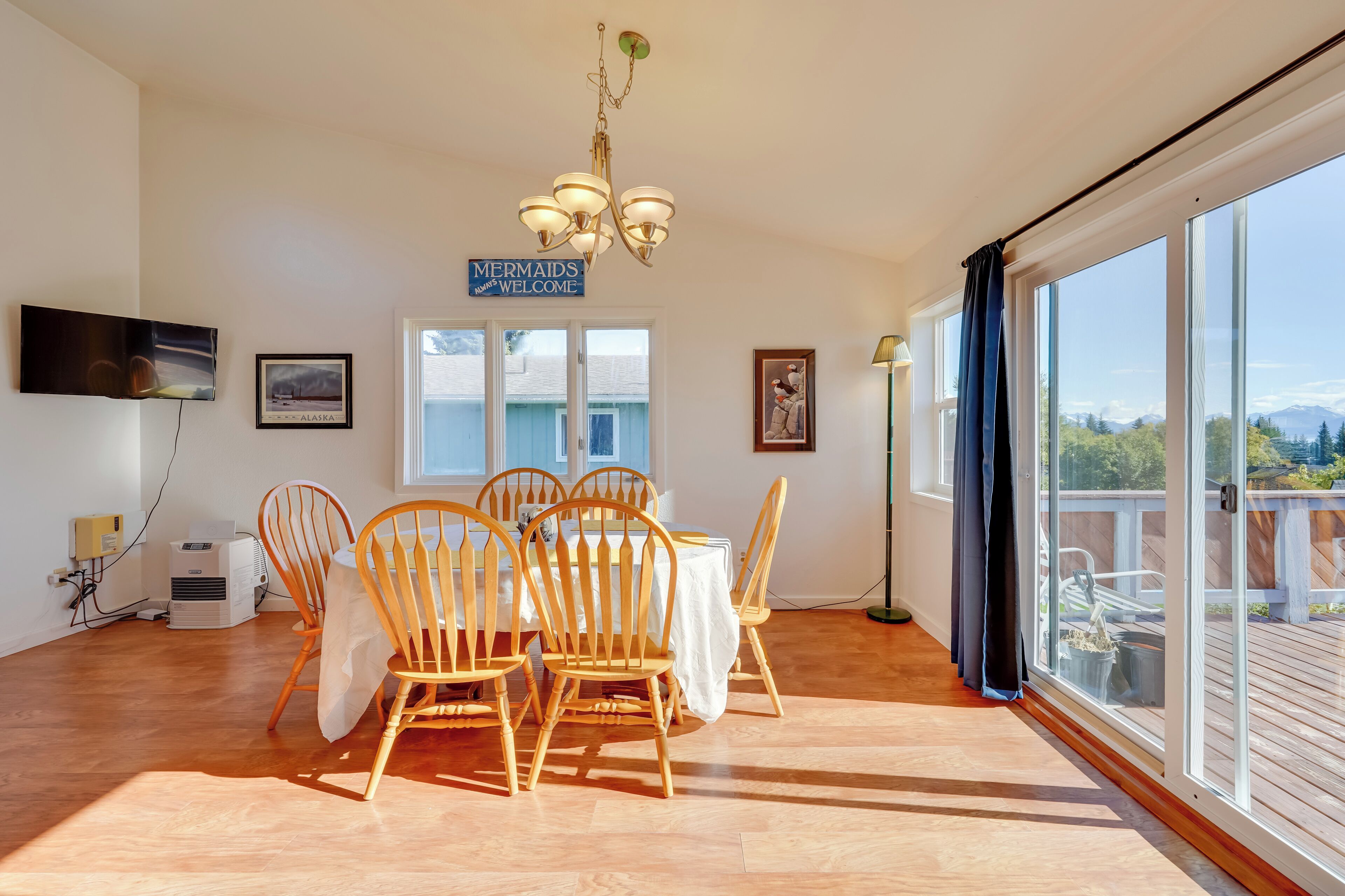 A dining area with a table and chairs, a chandelier, and a sign that reads "Mermaids Welcome".