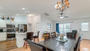 A modern kitchen with white cabinets, stainless steel appliances, and a dining area with a wooden table and chairs. - Golf + Poolside Bliss! Retreat 2 Mi to Lake Sumter (The Villages)