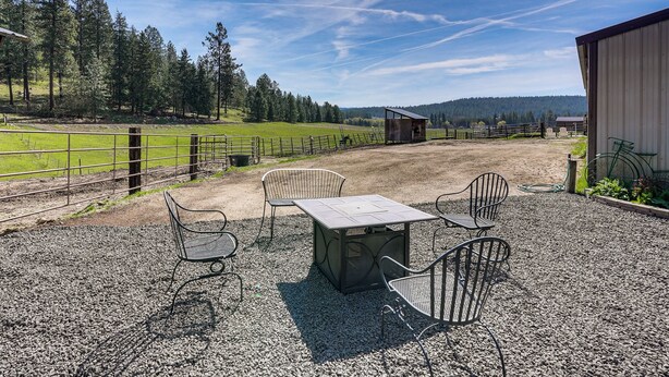 A gravel patio with metal chairs and a table, surrounded by a fenced pasture and trees. - Peaceful Farm Stay Near Spokane: Inland Hideaway! (Chattaroy)