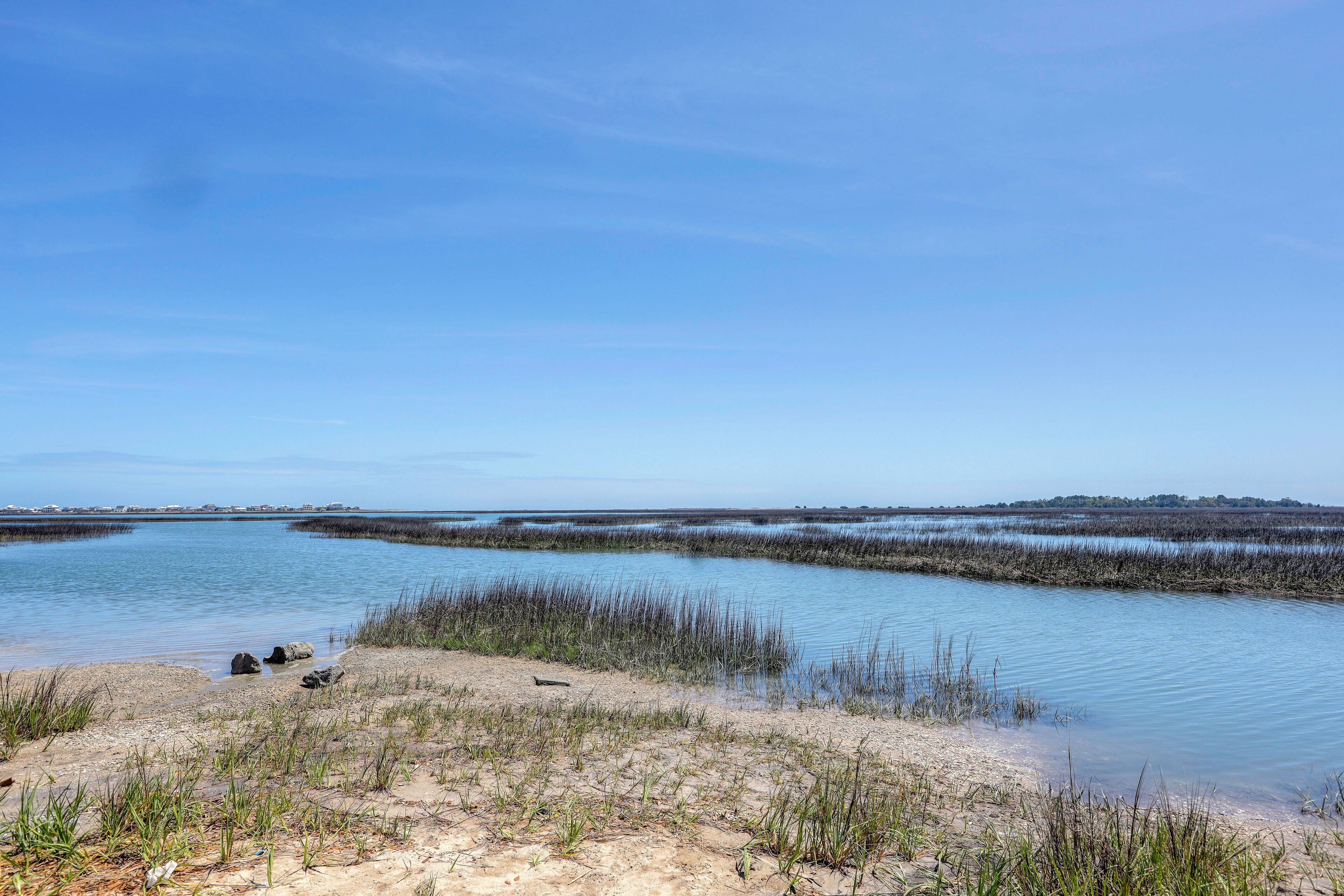 A coastal landscape with a sandy beach, shallow water, and sparse vegetation.