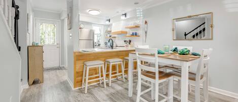 A modern kitchen with a wooden island, white bar stools, and a dining table.