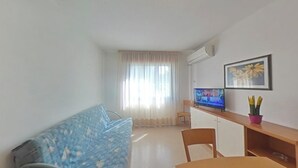 A small living area with a sofa, a TV, a desk, and a chair. - Inviting Flat Near the Beach and Main Shops (Lignano Sabbiadoro)