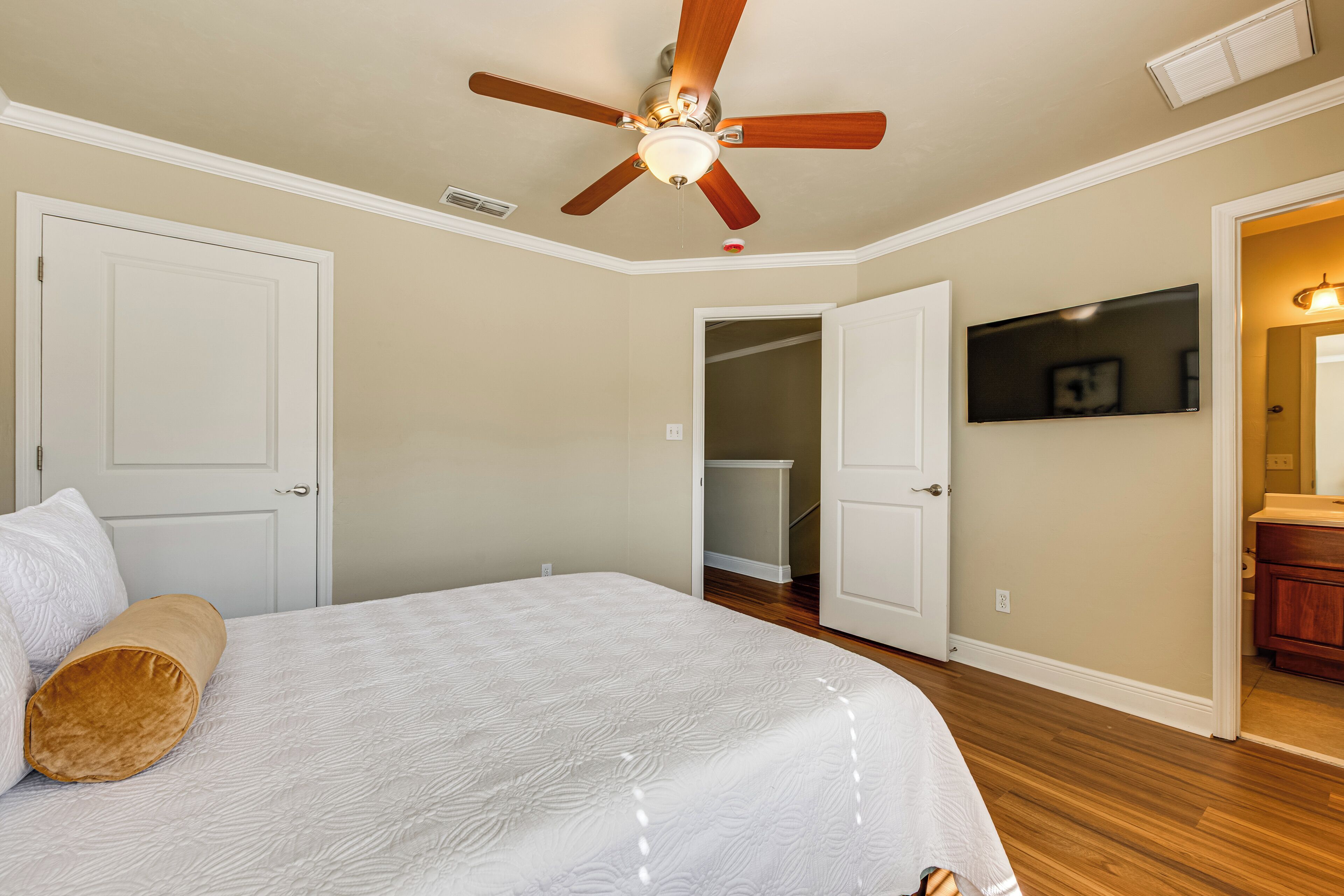 A bedroom with a bed, a ceiling fan, a TV, and an open closet.