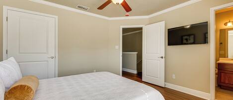 A bedroom with a bed, a ceiling fan, a TV, and an open closet.