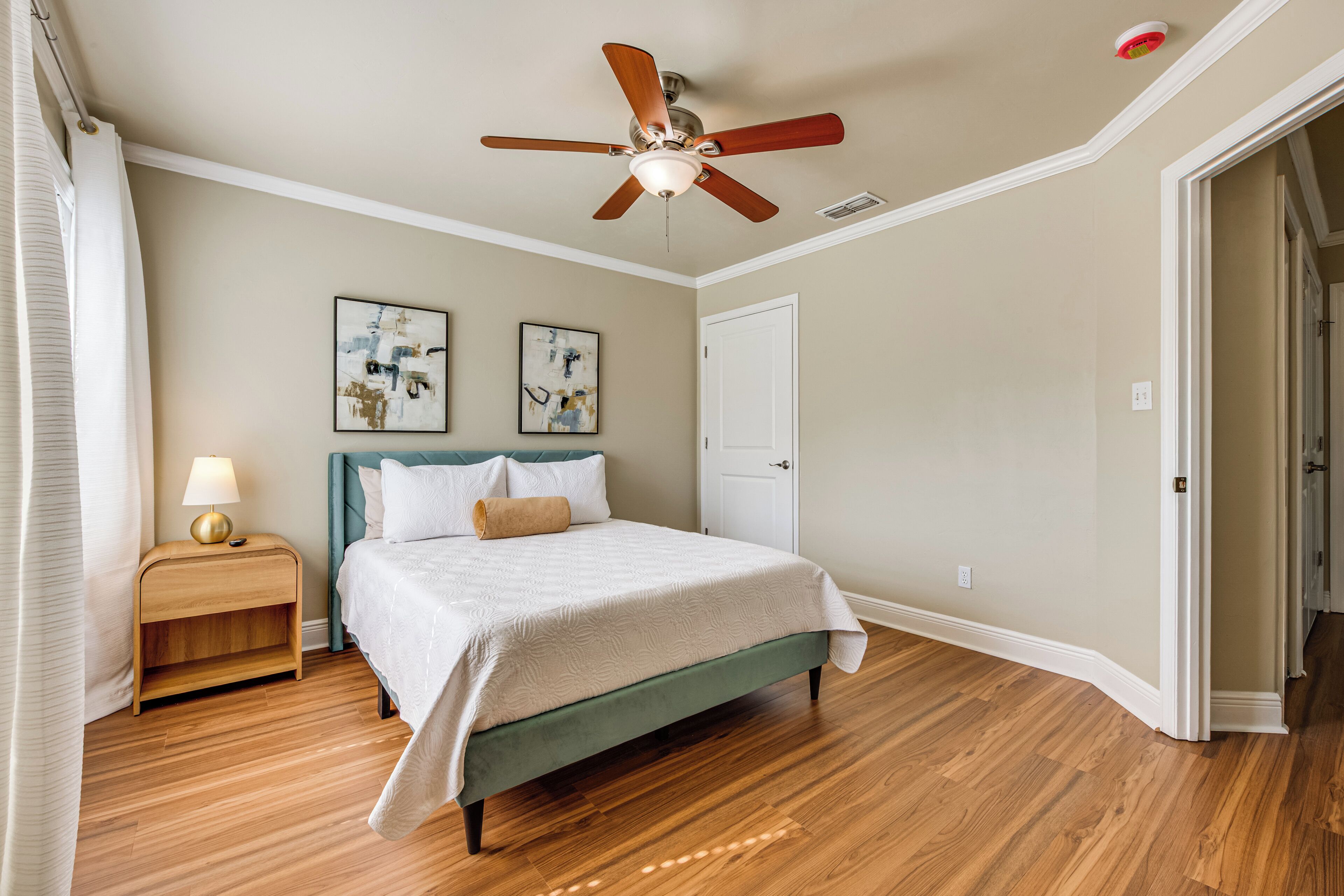 A bedroom with a bed, a nightstand, a ceiling fan, and two wall-mounted artworks.