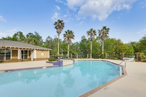 Ein Swimmingpool mit einer gefliesten Kante, ein überdachter Bereich mit Dach und Palmen im Hintergrund.