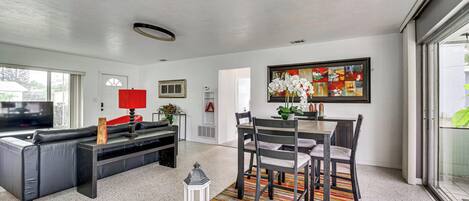 A modern living room with a sofa, TV, dining table, chairs, and a colorful rug.