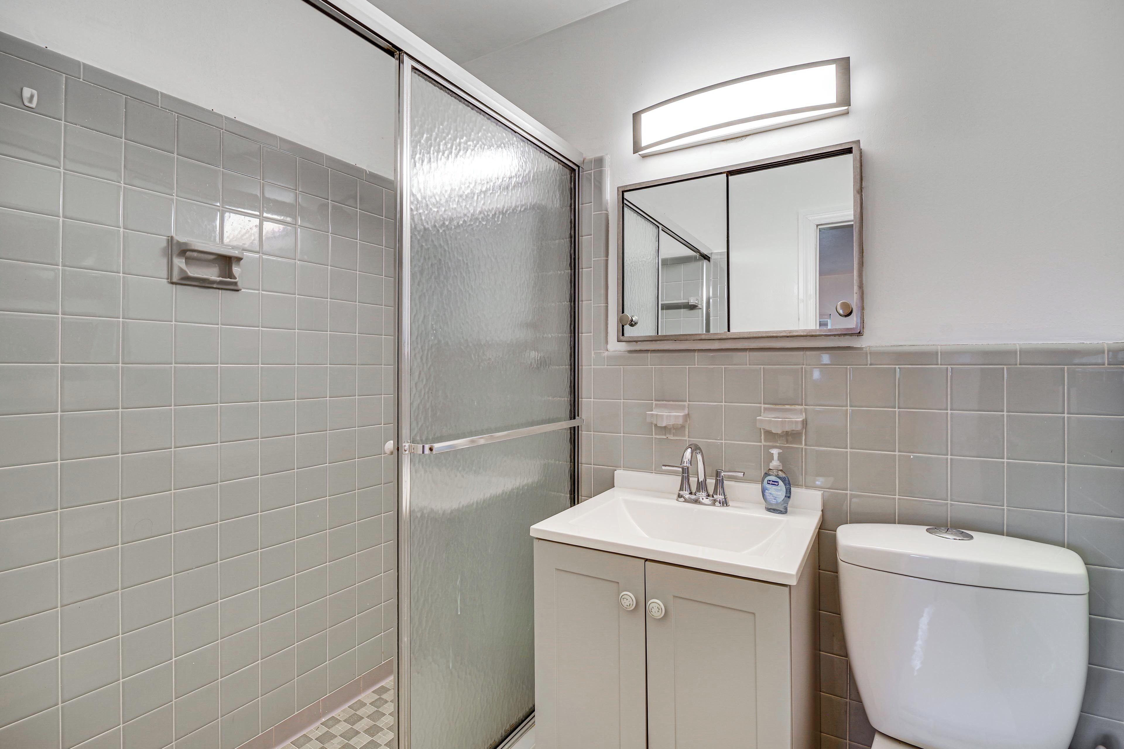 A bathroom with a shower, sink, toilet, and a mirror.