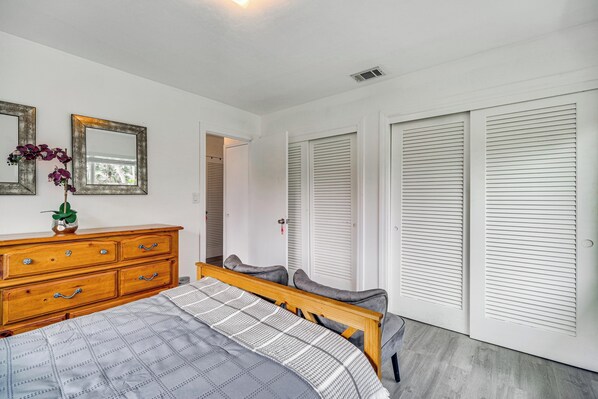 Une chambre à coucher comprenant un lit, une commode, deux miroirs et un placard avec des portes à persiennes.