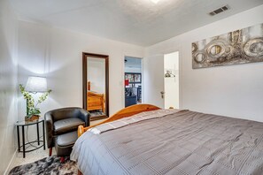 Ein Schlafzimmer mit einem Bett, einem Sessel, einer Lampe und einem Bild an der Wand.
