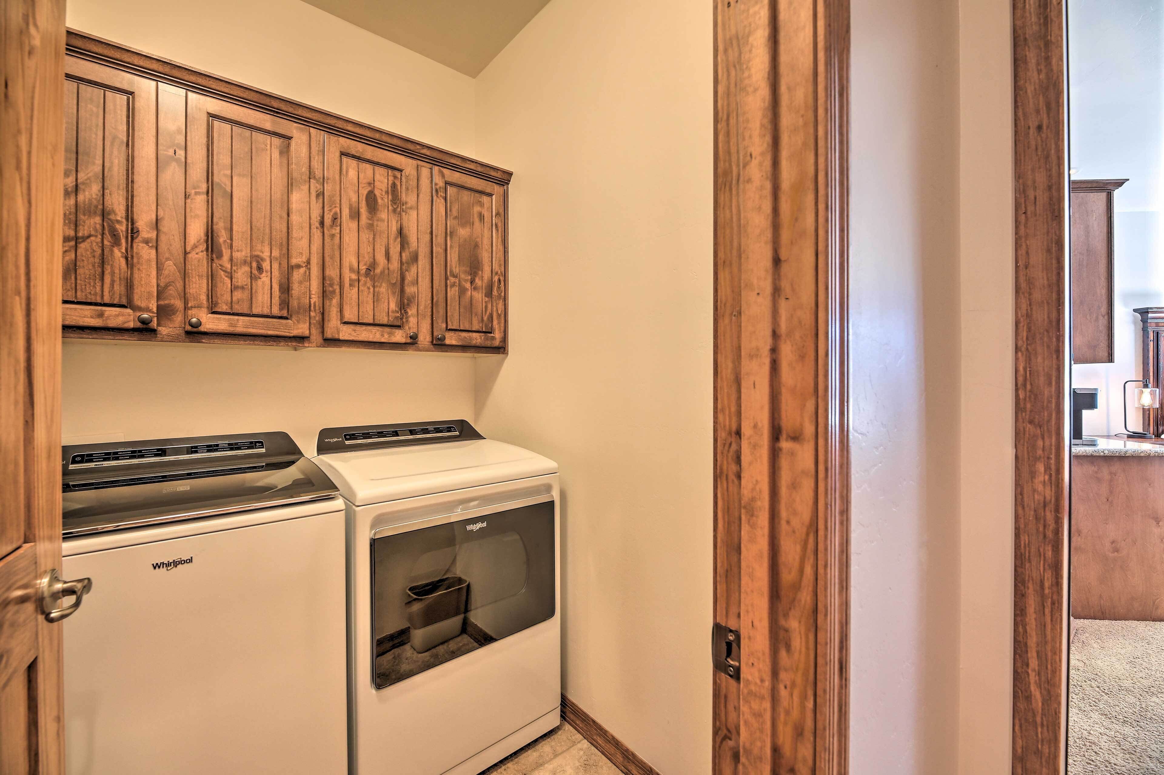 A laundry room with a Whirlpool washer and dryer, wooden cabinets, and a wooden door.