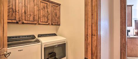 A laundry room with a Whirlpool washer and dryer, wooden cabinets, and a wooden door.