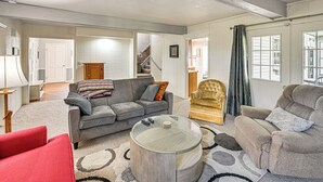 Un salon avec un canapé gris, un fauteuil rouge, une table basse en verre et un tapis à motifs.