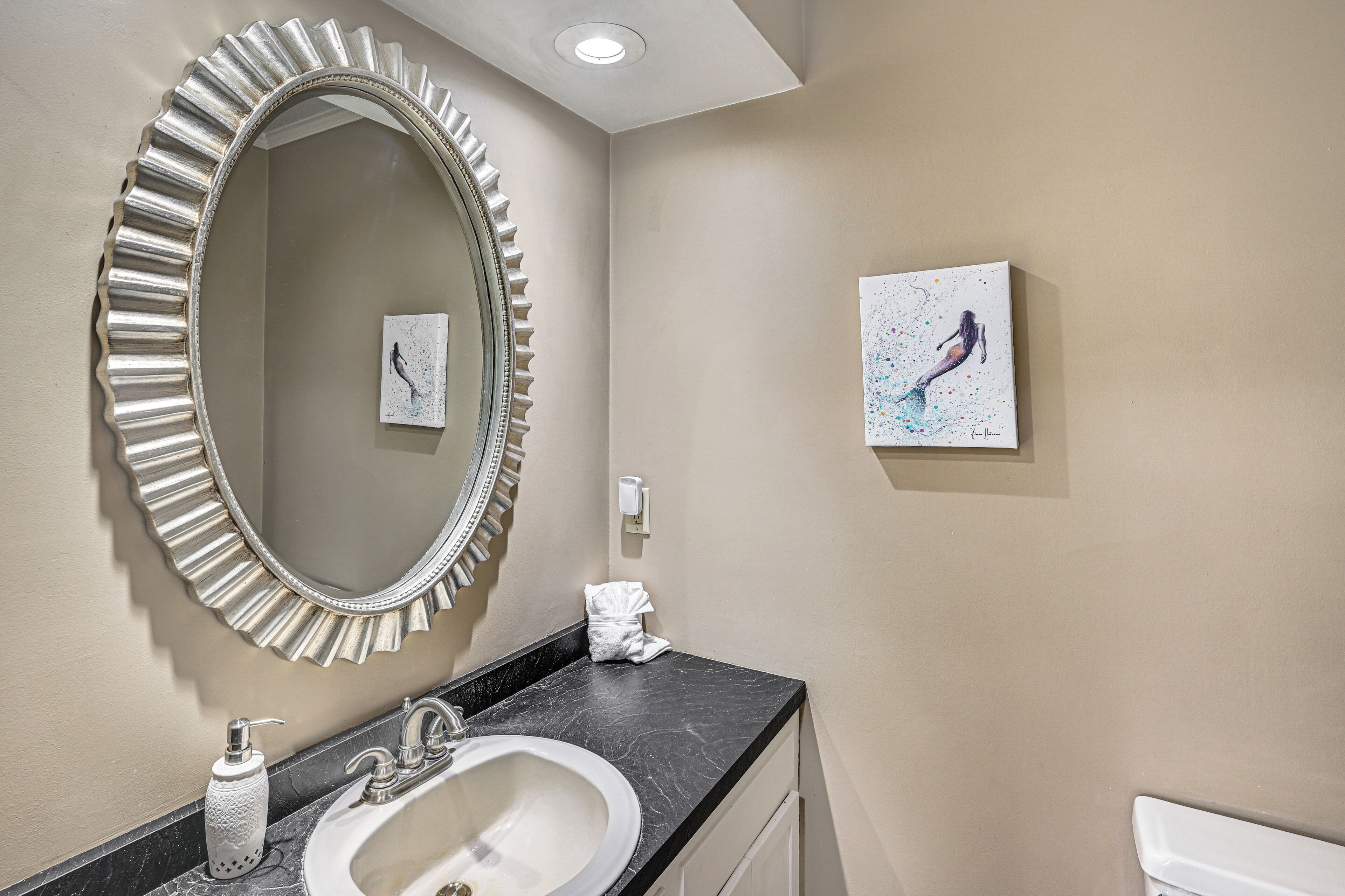 A bathroom with a large mirror, a sink, a towel, and a painting on the wall.