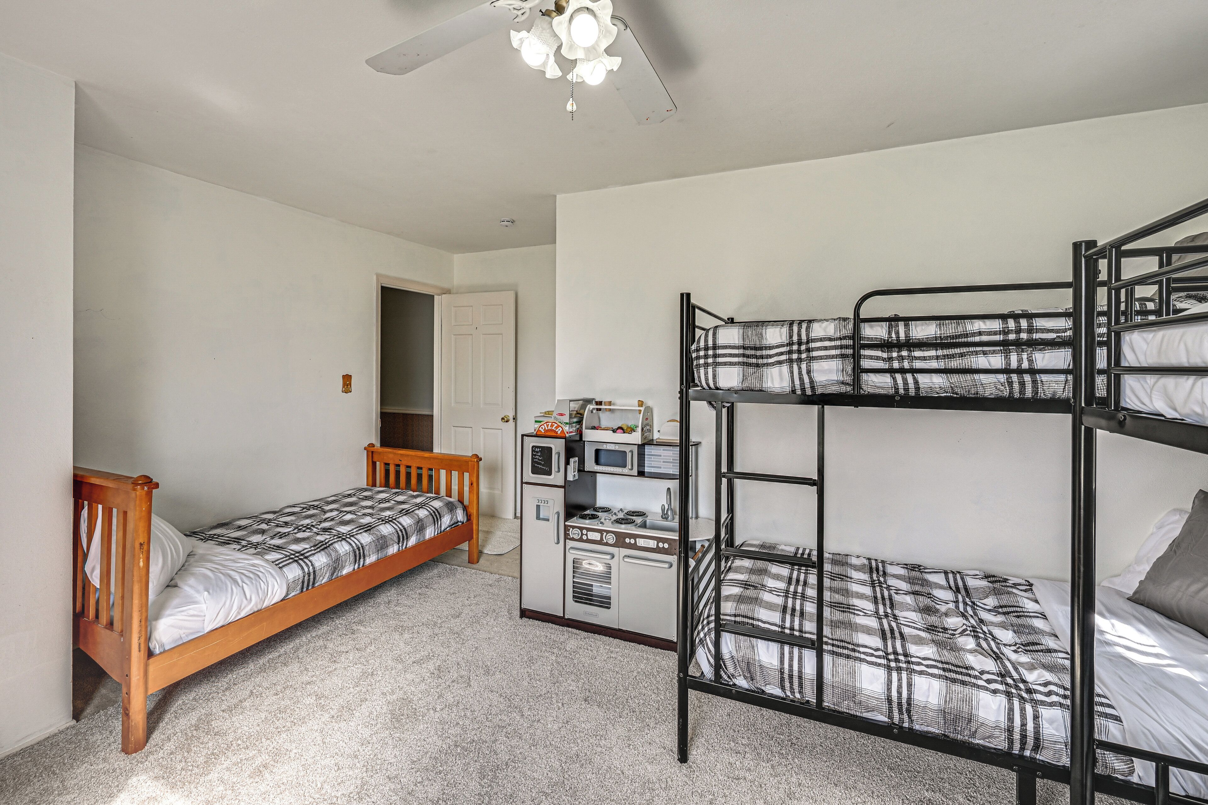 A room with bunk beds, a wooden bed, a kitchenette, and a ceiling fan.
