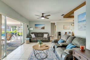 A living room with a ceiling fan, a sofa, a coffee table, and a view through a glass door. - Private Yard + Heated Pool: Port Charlotte Oasis (Port Charlotte)