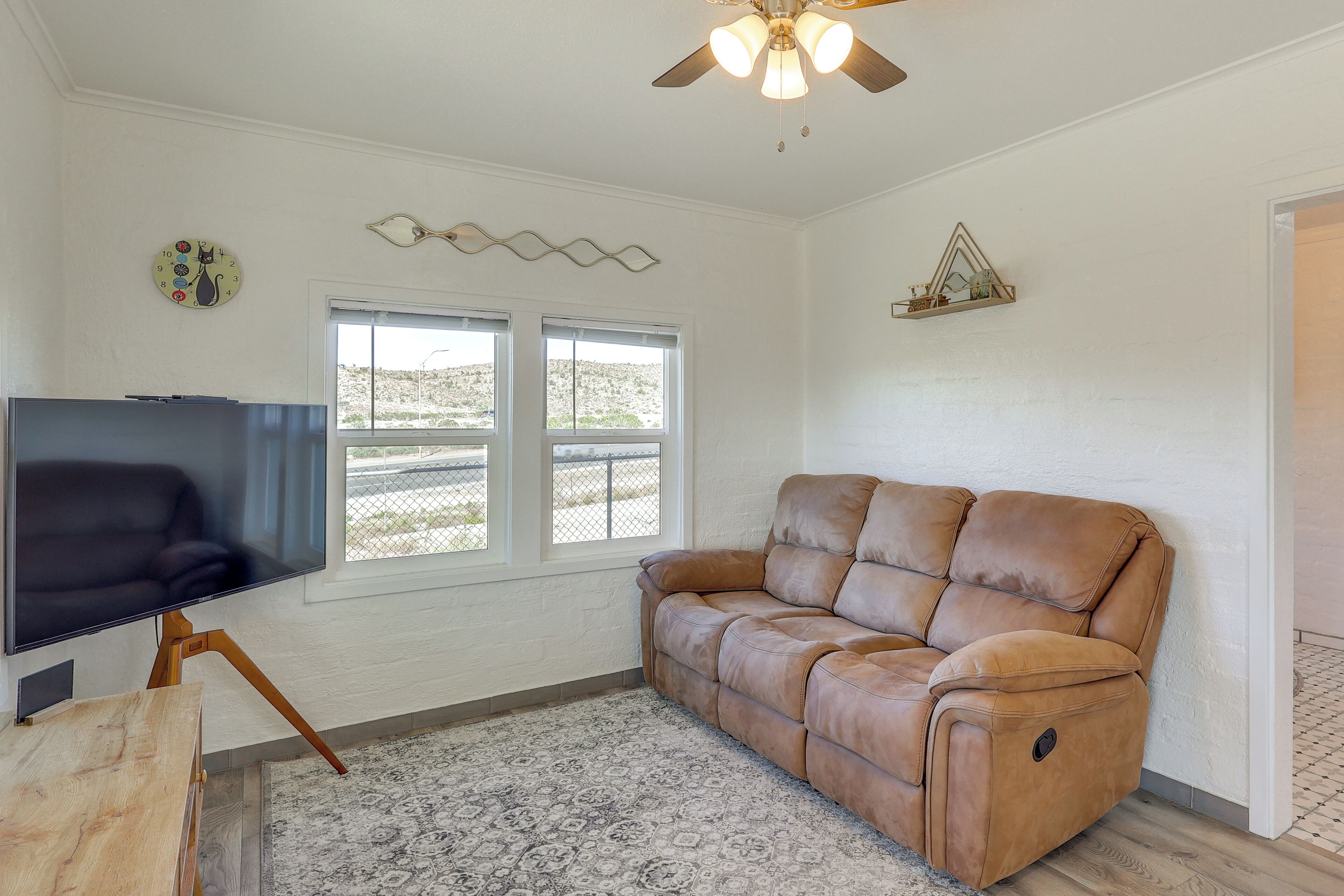 A living room with a leather sofa, a flat-screen TV on a wooden stand, a patterned rug, and a ceiling fan.