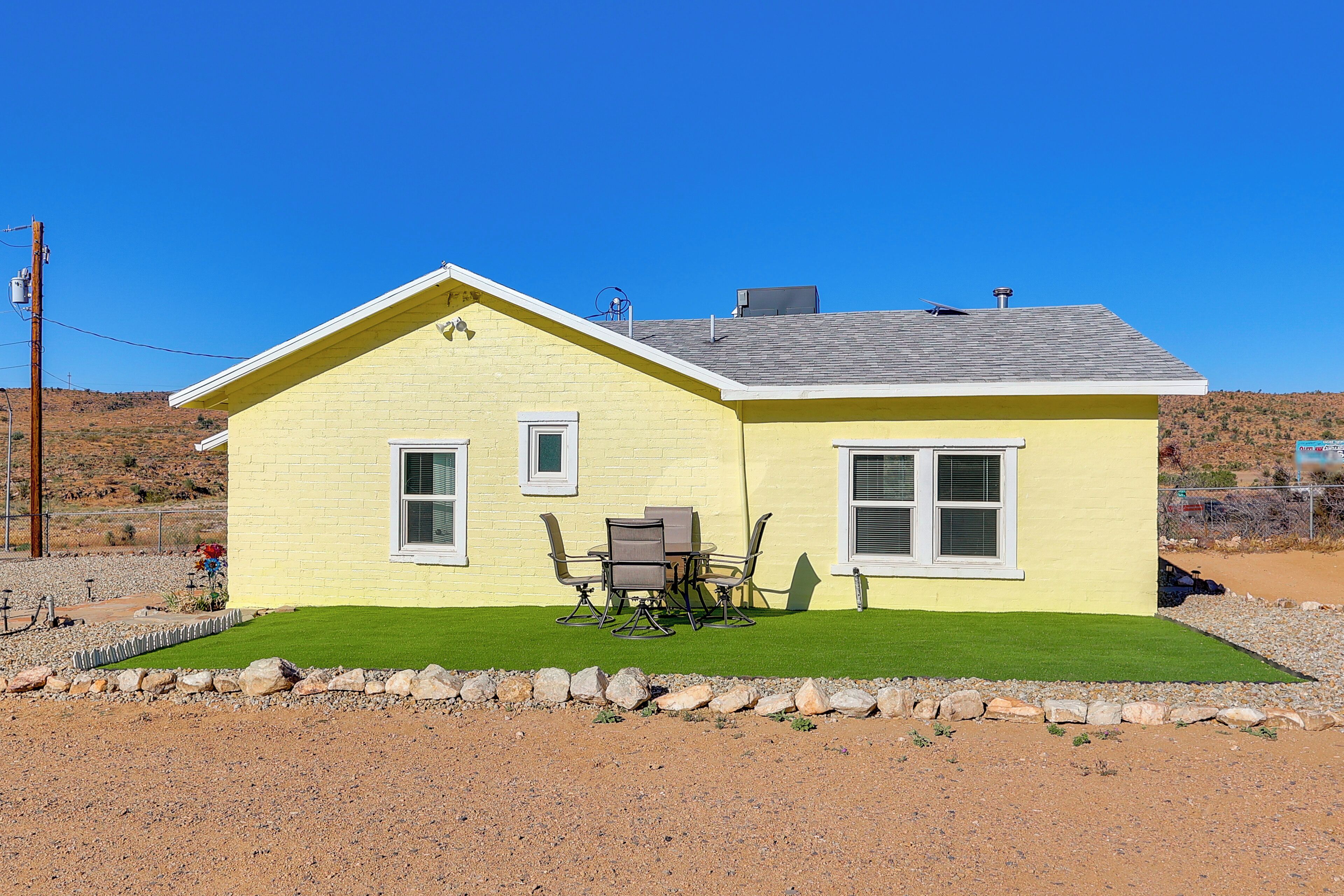 A yellow single-story house with a small patio, a table with chairs, and a well-maintained lawn.