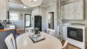 Een keuken met witte kasten, een eettafel met stoelen, een kroonluchter en een wasmachine.