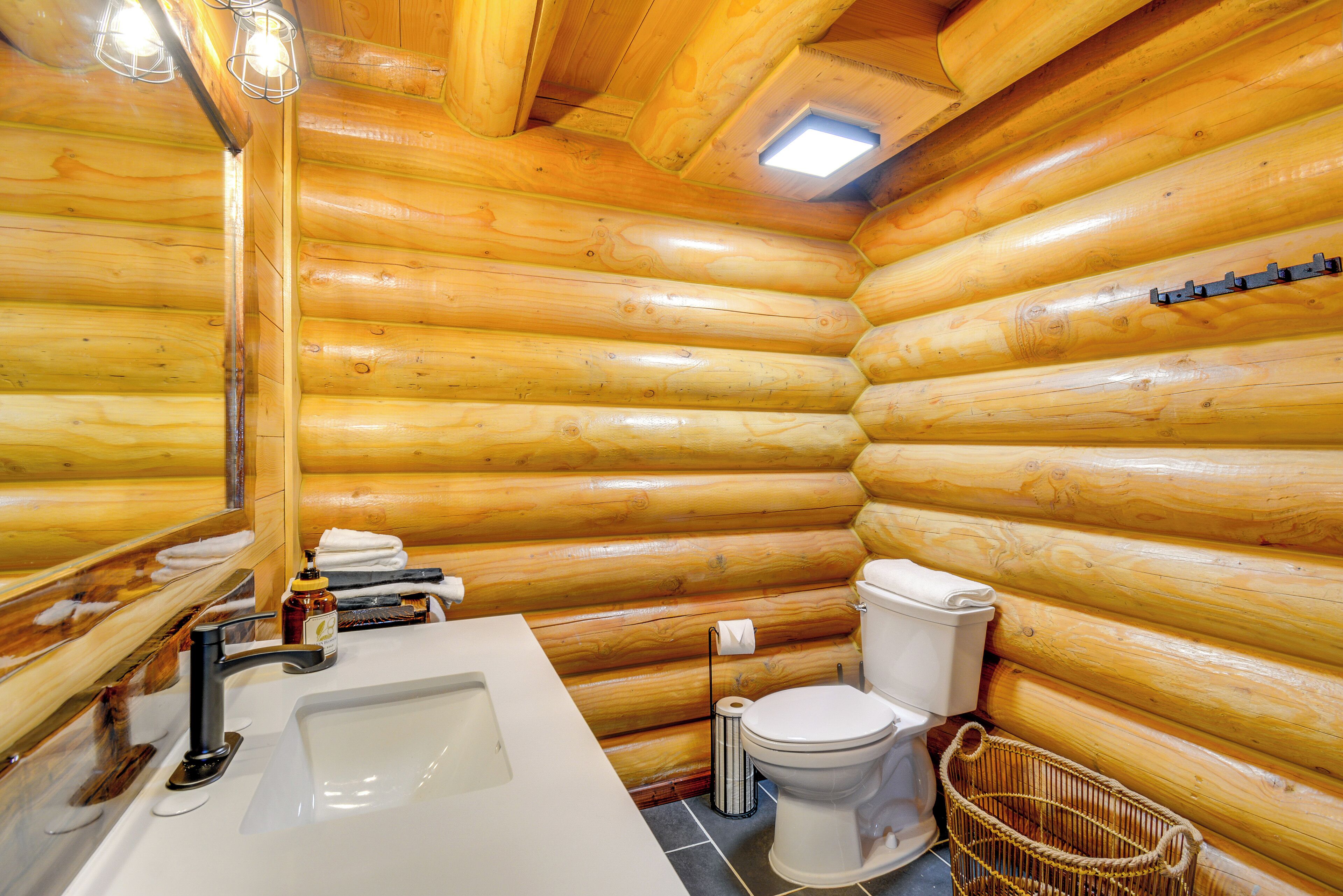 A log cabin bathroom with a sink, toilet, and mirror.