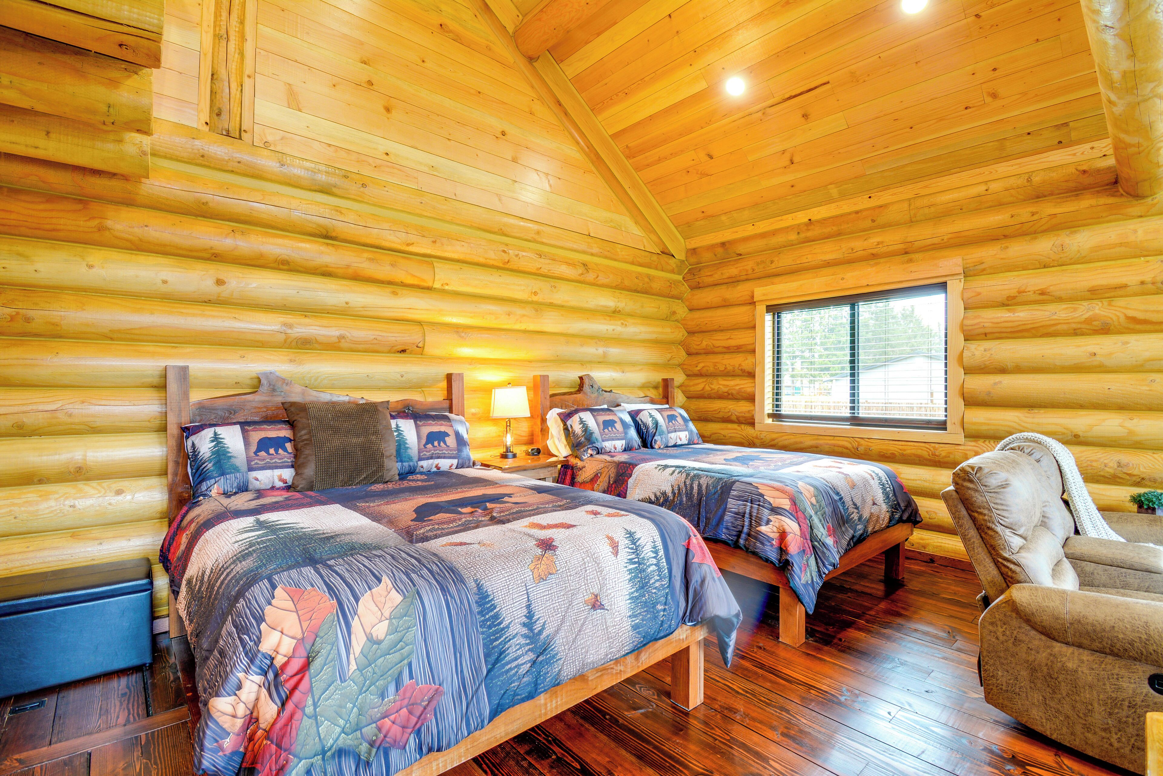 A log cabin bedroom with two beds, a chair, and a window.