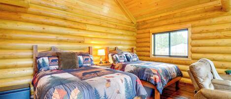 A log cabin bedroom with two beds, a chair, and a window.