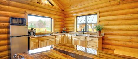 Une cuisine rustique aménagée dans une cabane en rondins, avec des murs en bois, un réfrigérateur, un four à micro-ondes, un évier et une grande fenêtre.