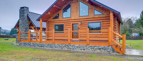 A log cabin with a stone chimney, large windows, and a wooden deck.