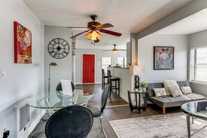 Una sala moderna con una mesa de comedor de vidrio, un sofá, un ventilador de techo y una puerta roja al fondo.