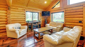 Interior de una cabaña de troncos con techo de madera, sofás de cuero, una mesa de centro y un televisor.