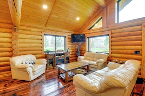 A log cabin interior with a wooden ceiling, leather sofas, a coffee table, and a television.
