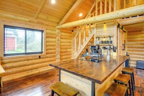 A log cabin interior with a wooden bar area, a staircase, and a kitchen.