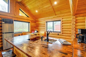 A wooden cabin interior with a kitchen area featuring a stainless steel refrigerator, a microwave, a sink, and a coffee maker.