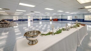 Un vaste hall où une longue table est dressée pour un événement officiel, agrémentée d’un saladier en argent et de décorations florales.