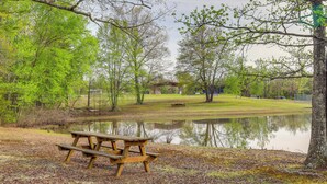 Une table de pique-nique près d’un étang, avec des arbres et un kiosque en arrière-plan.