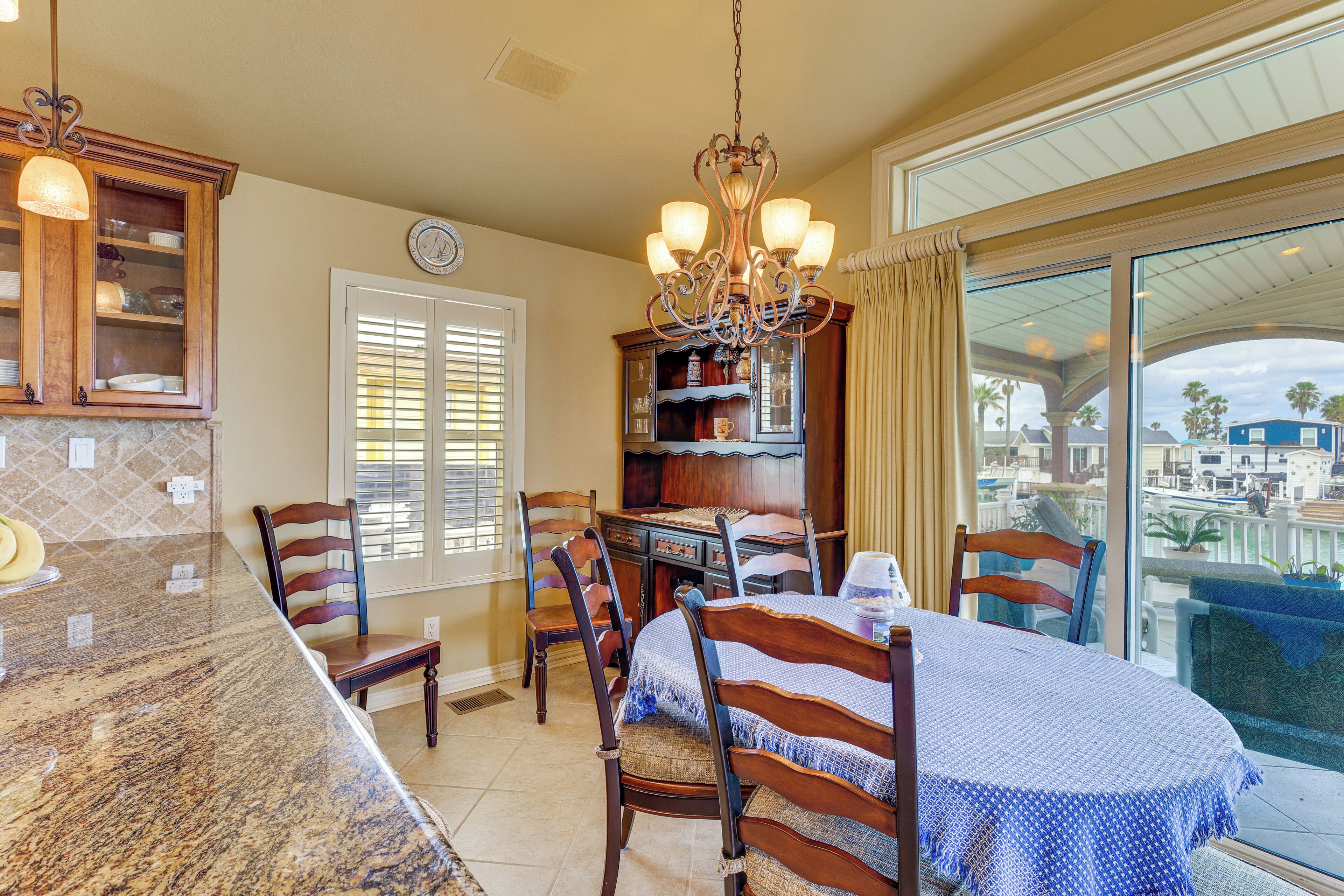 A kitchen with a granite countertop, wooden chairs, a chandelier, and a dining table with a blue tablecloth.