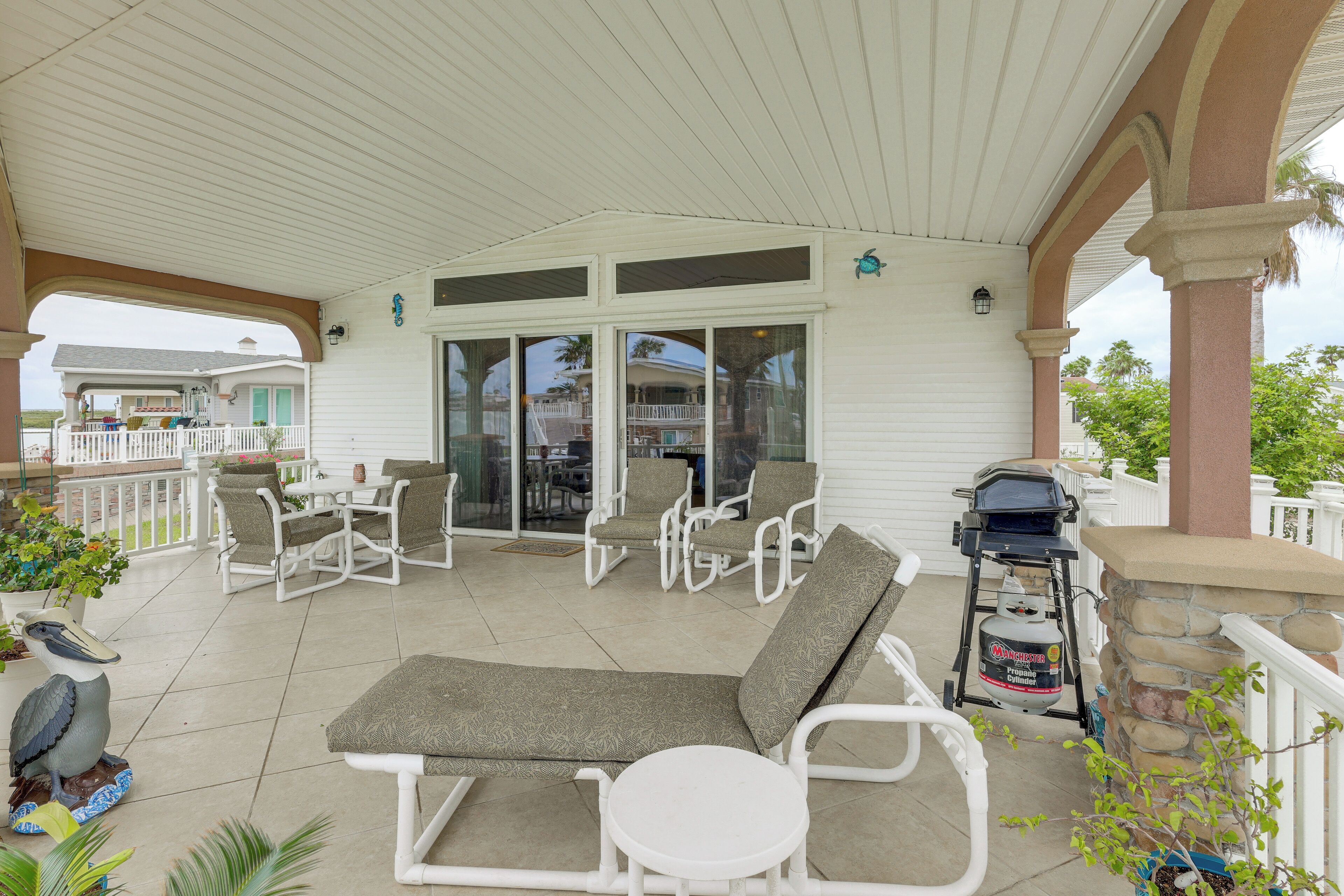 A covered patio with lounge chairs, a grill, and a view of the house.