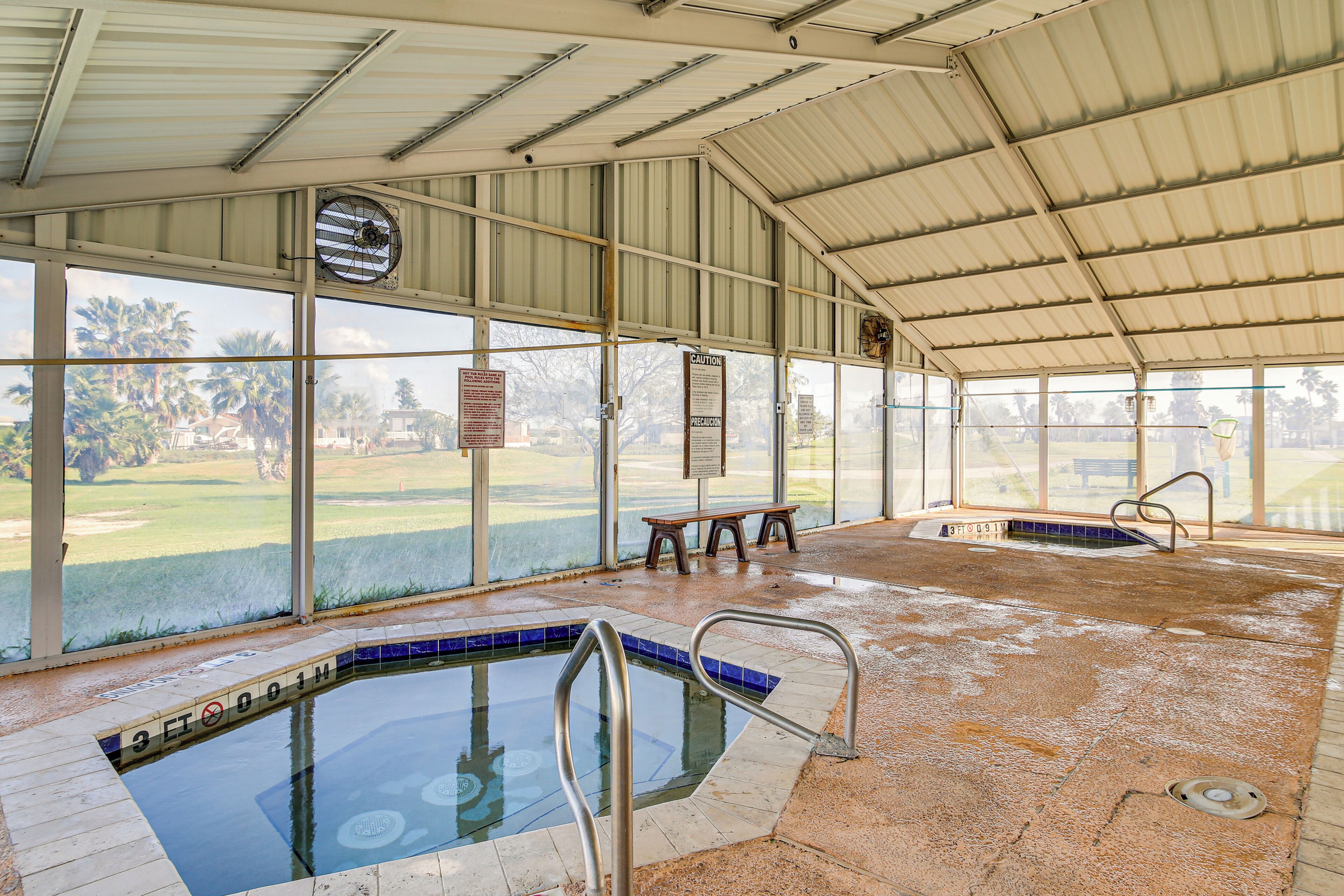 An indoor swimming pool with clear glass walls, a bench, and a safety sign.