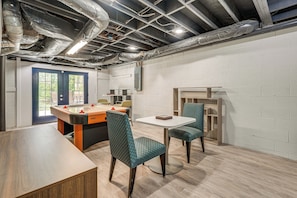 A room with a pool table, two chairs, a table, and a door.