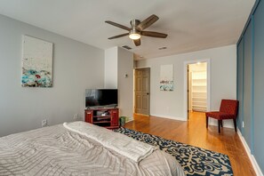 A bedroom with a bed, a ceiling fan, a TV, a red chair, and a hallway leading to a closet. - Smyrna Sanctuary Near Parks: Spacious Yard + Deck (Smyrna)
