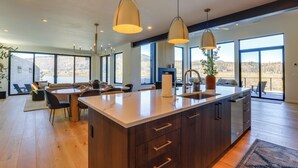 A modern kitchen with a large island, pendant lights, and a view of the outdoors.
