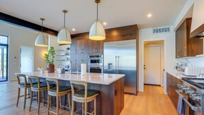 A modern kitchen with a central island, bar stools, pendant lighting, stainless steel appliances, and wooden cabinetry.